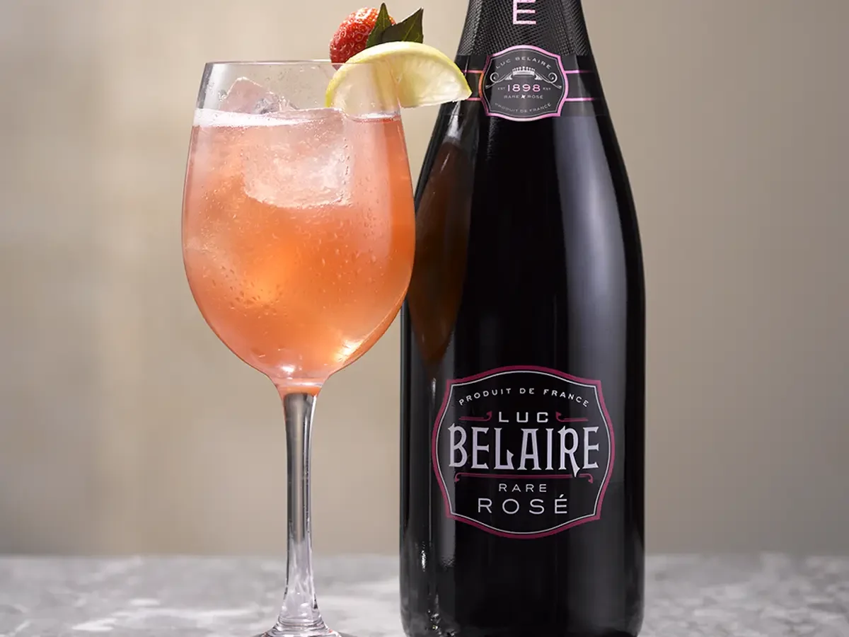 Belaire Rare Punch cocktail in a highball glass with ice and a grapefruit garnish, served beside a bottle of Luc Belaire Rare Rosé.
