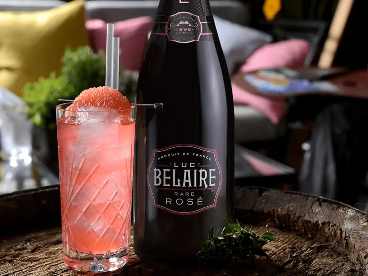 Cote D'Azur Spritz cocktail in a wine glass garnished with strawberry, mint, and lemon, served beside a bottle of Luc Belaire Rare Rosé.